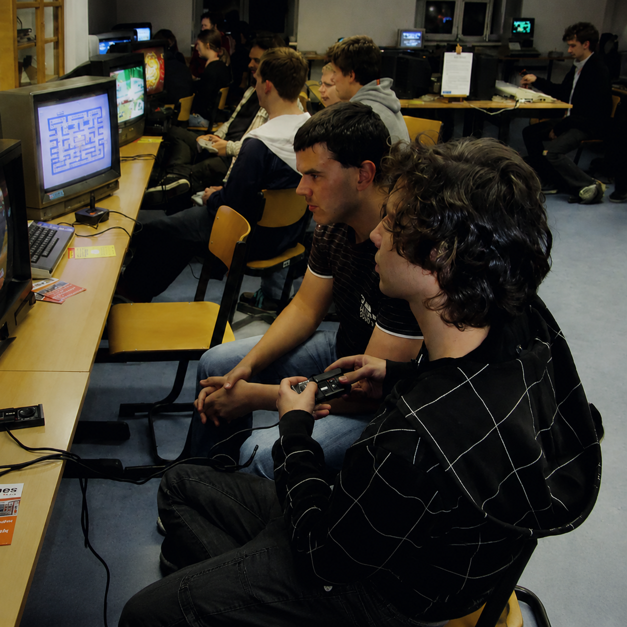 „Our Story“-Bild mit Retro-Gamern in einem Community-Raum, die mit Controllern und CRT-Fernsehern klassische Spiele spielen.